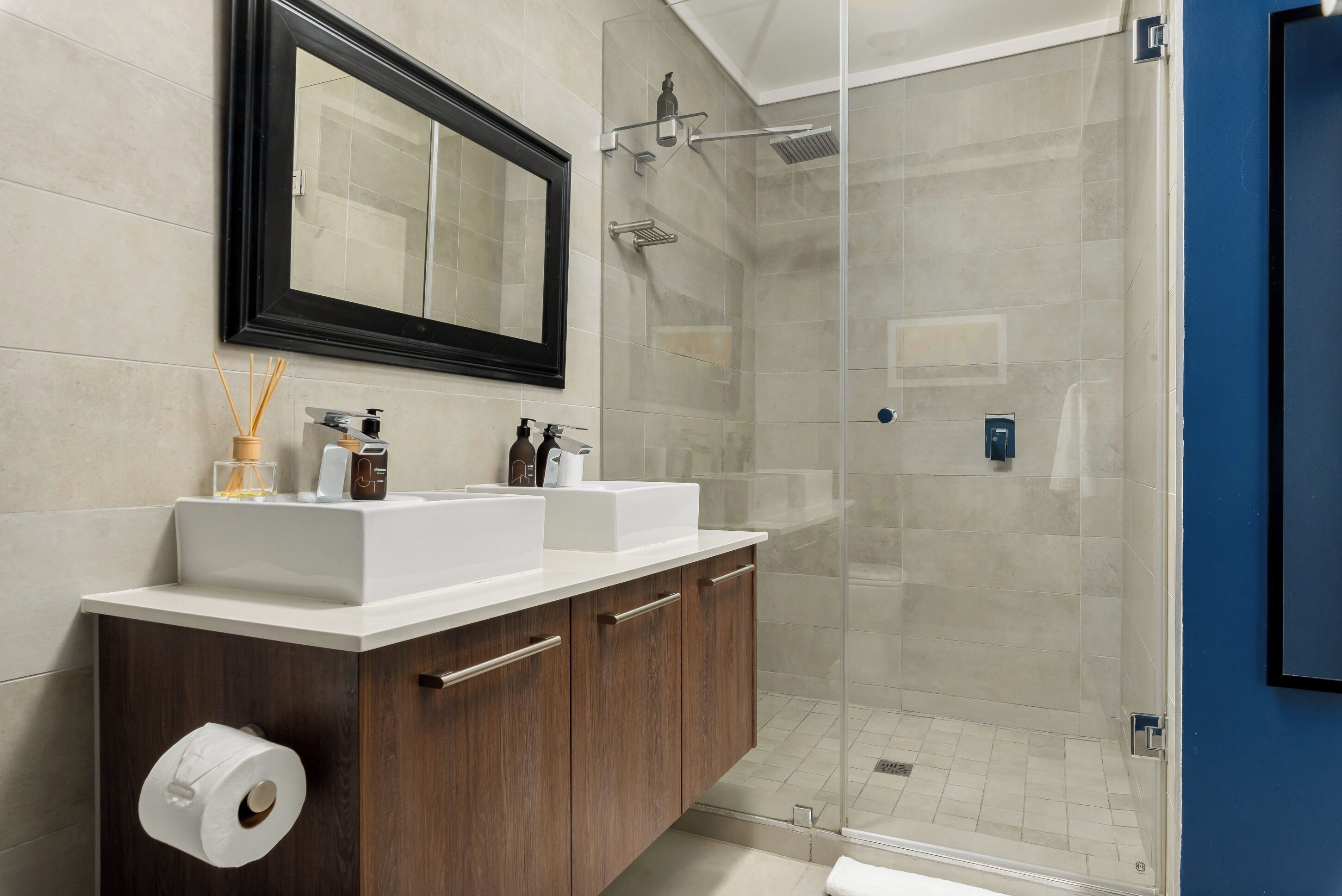 A modern bathroom with a large mirror, dual sinks, a shower enclosure, and a dark wooden vanity.