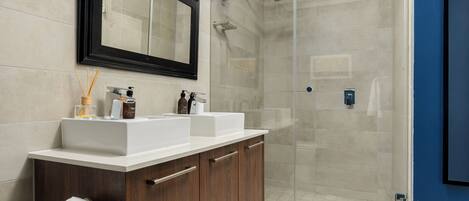 A modern bathroom with a large mirror, dual sinks, a shower enclosure, and a dark wooden vanity.