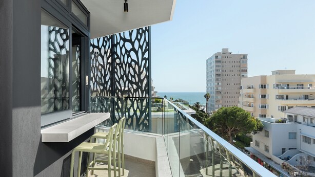 Un balcón con barandilla de cristal, vista al mar y una celosía metálica decorativa.