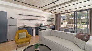 A modern living space with a sofa, armchair, and dining table. A kitchen area with cabinets and a refrigerator is visible.