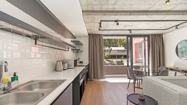 A modern kitchen with stainless steel appliances, a dining area with a round table, and a view of the outdoors through large windows.