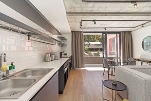 A modern kitchen with stainless steel appliances, a dining area with a round table, and a view of the outdoors through large windows.