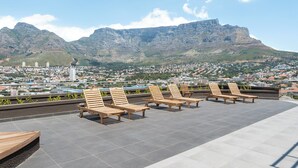A rooftop terrace with wooden lounge chairs and a city view.