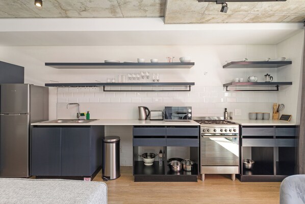 A modern kitchen with a built-in oven, microwave, and sink. There are black cabinets and a stainless steel trash can.