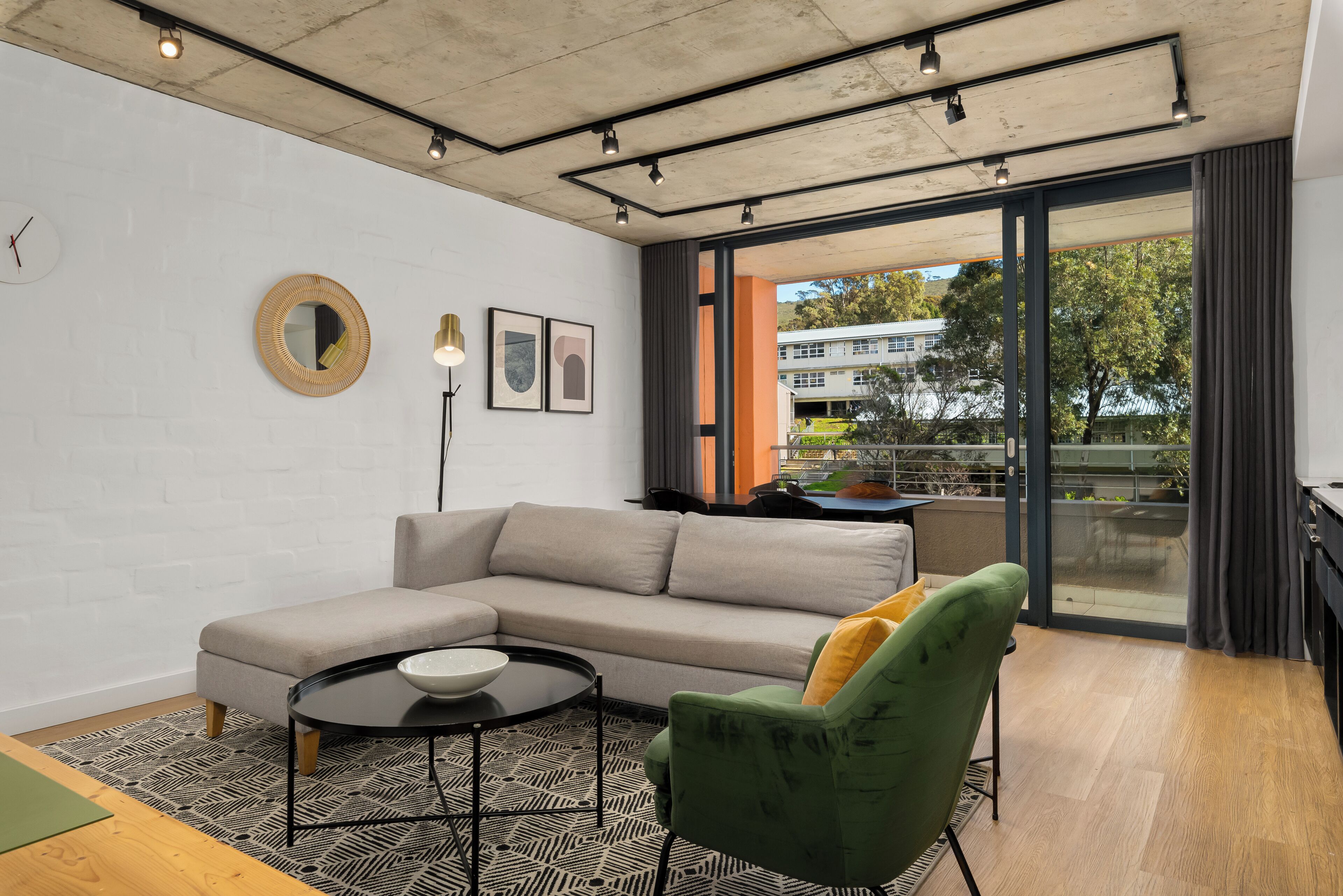 A modern living room with a sectional sofa, a round mirror, framed artwork, and a view through a glass door.