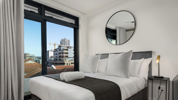 A modern hotel room with a large bed, a round mirror, and a view of the cityscape. - The Sage l Elegant Studio in Vibrant Sea Point (Cape Town)