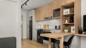 A modern kitchen with wooden cabinets, a built-in oven, and a dining area with a wooden table and chairs. - The Sage l Elegant Studio in Vibrant Sea Point (Cape Town)