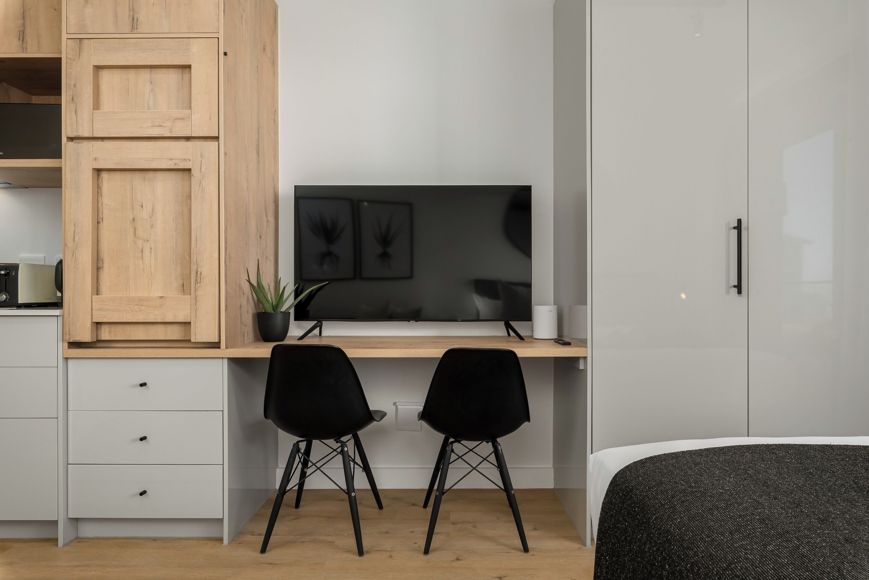 A modern bedroom with a bed, a desk with two black chairs, a TV, and a wardrobe.