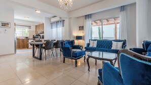 Uma sala de estar moderna com um sofá azul, uma área de jantar com mesa e cadeiras, e uma cozinha ao fundo.