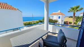 A balcony with a table and chair, overlooking a coastal area with a clear view of the sea and a white building with a red roof. - Seaview Sanctuary House (Agios Theodoros)
