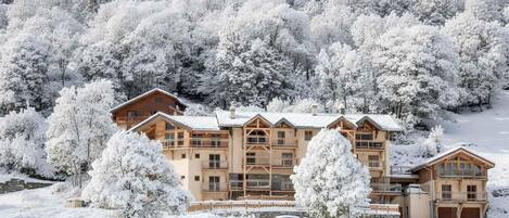 A multi-story lodge with a wooden exterior, surrounded by snow-covered trees and a clear sky.