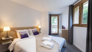 Una habitació d'hotel amb un llit gran, dues taules de nit amb làmpades, una finestra amb cortines i vistes a verdura a l'exterior.