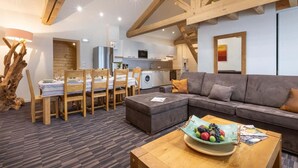 Een moderne woonkamer met een bank, eettafel en stoelen. Achtergrond toont een keuken met een wasmachine.