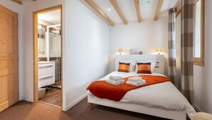 Een slaapkamer met een bed, een houten deur, een badkamer met een spiegel en een raam.