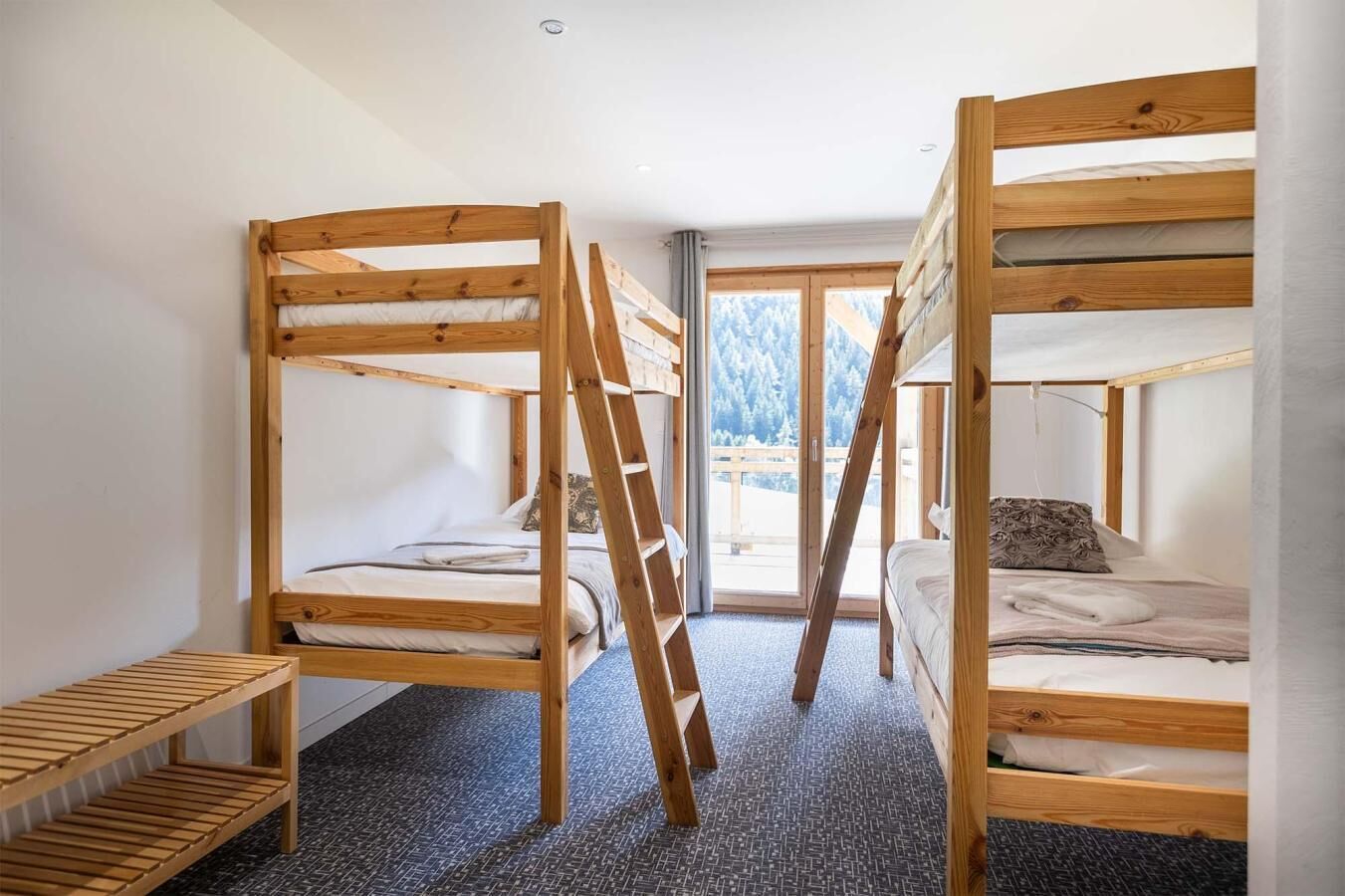 Una habitación con tres literas de madera, un pequeño estante de madera y una ventana con vistas a árboles.