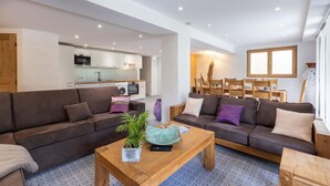 A modern living room with a sofa set, a coffee table with a plant, and a dining area with wooden chairs and a table.