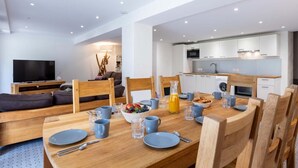 A modern living room with a TV, sofa, and dining area with a table set for four.