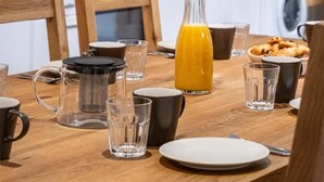 A modern kitchen with white cabinets, a wooden dining table set with plates, glasses, and a pitcher of orange juice.
