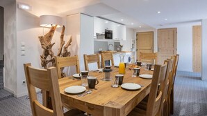 A modern dining area with a wooden table set for four, surrounded by wooden chairs. A unique wooden sculpture decorates the wall.