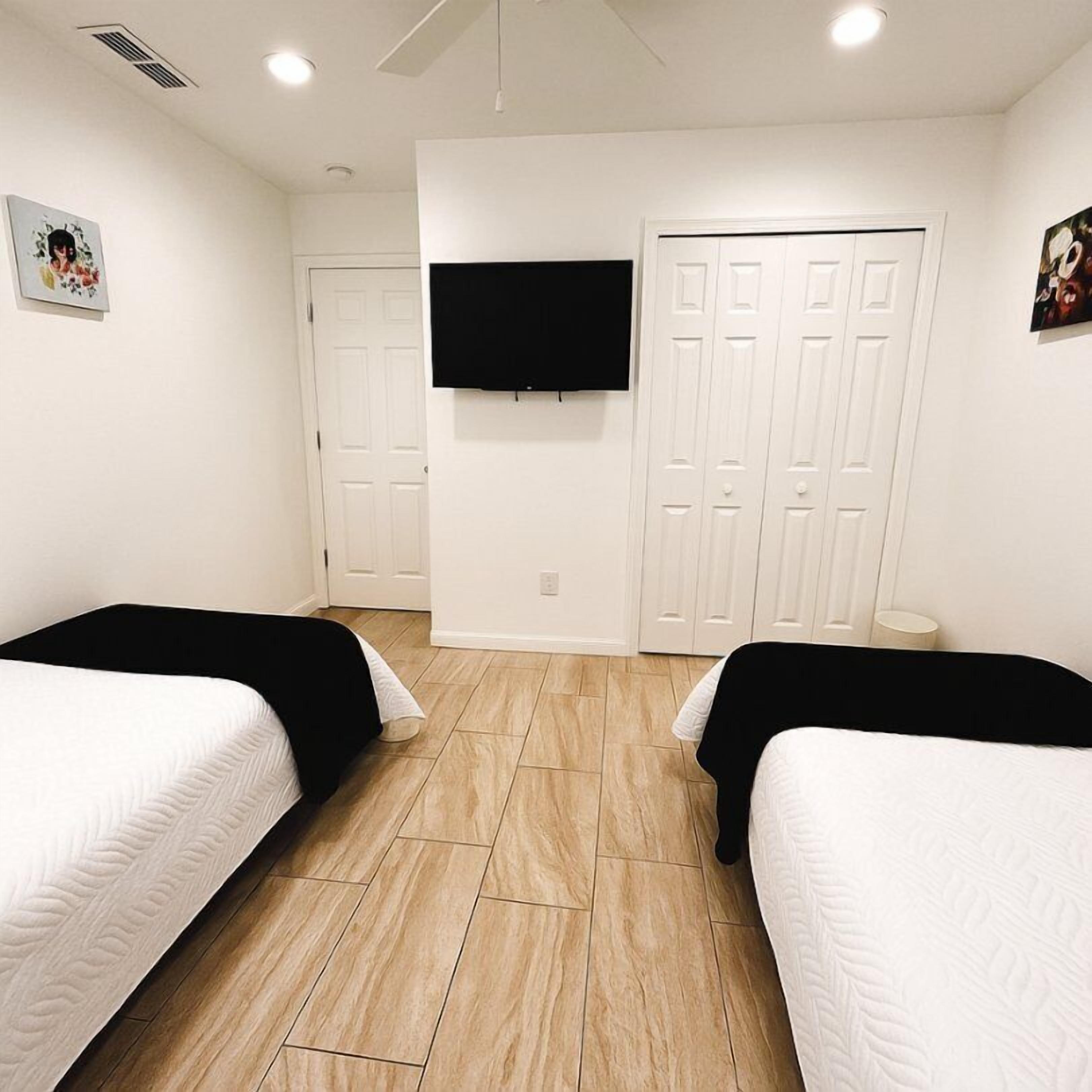 A room with two beds, a TV mounted on the wall, and a set of white doors.