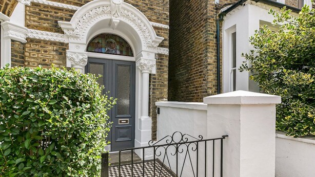 A traditional brick house with a dark blue door, white decorative archway, and a gated entrance with a black metal gate. - Elegant GetAway House in Vibrant Clapham Juction - Pass the Keys (London)
