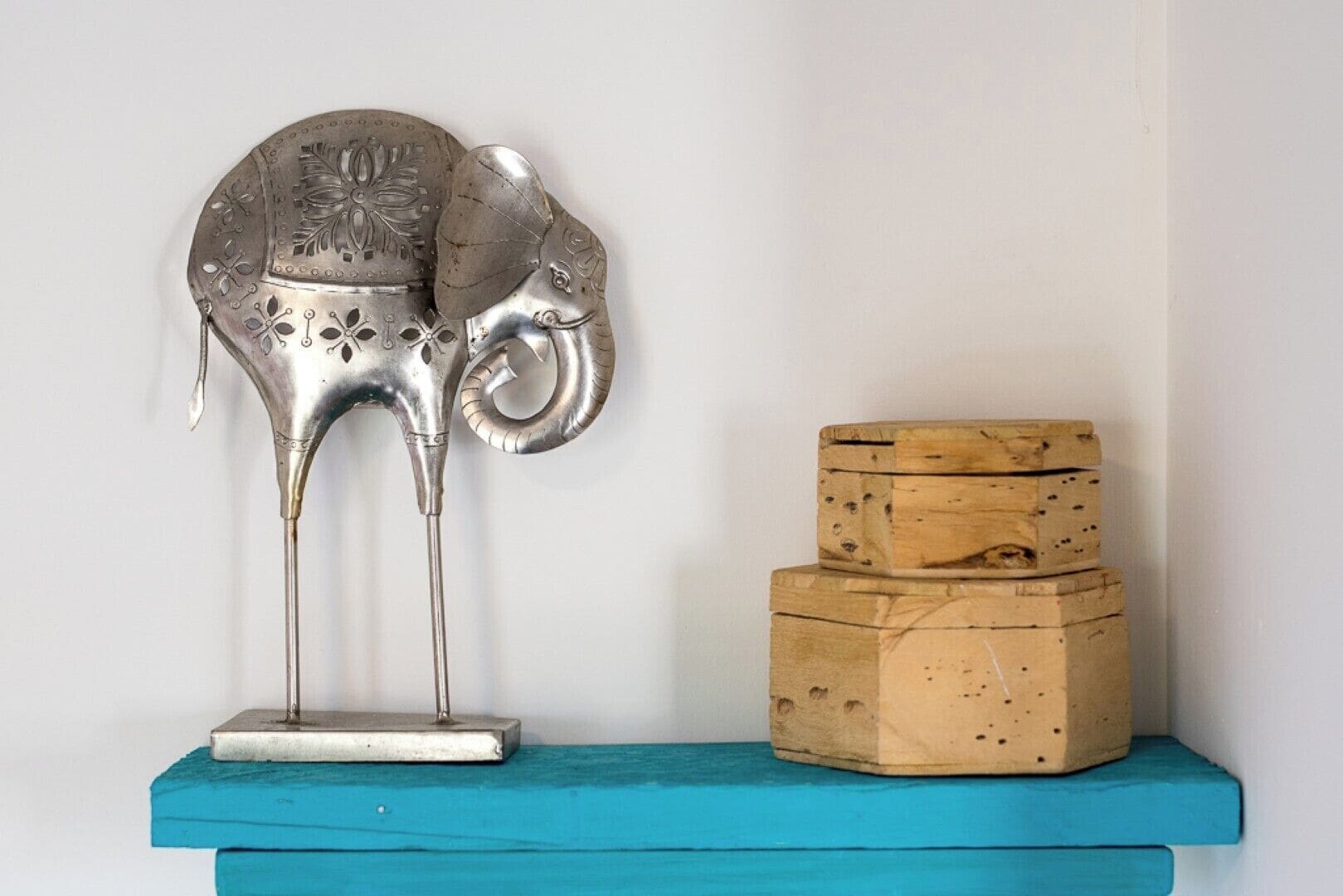A metal sculpture of an animal on a blue shelf next to two wooden boxes.