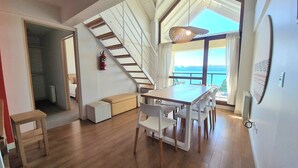 A spacious room with a wooden floor, a dining table with chairs, a staircase, and a view of the sea. - Terrazas I y II (San Carlos de Bariloche)