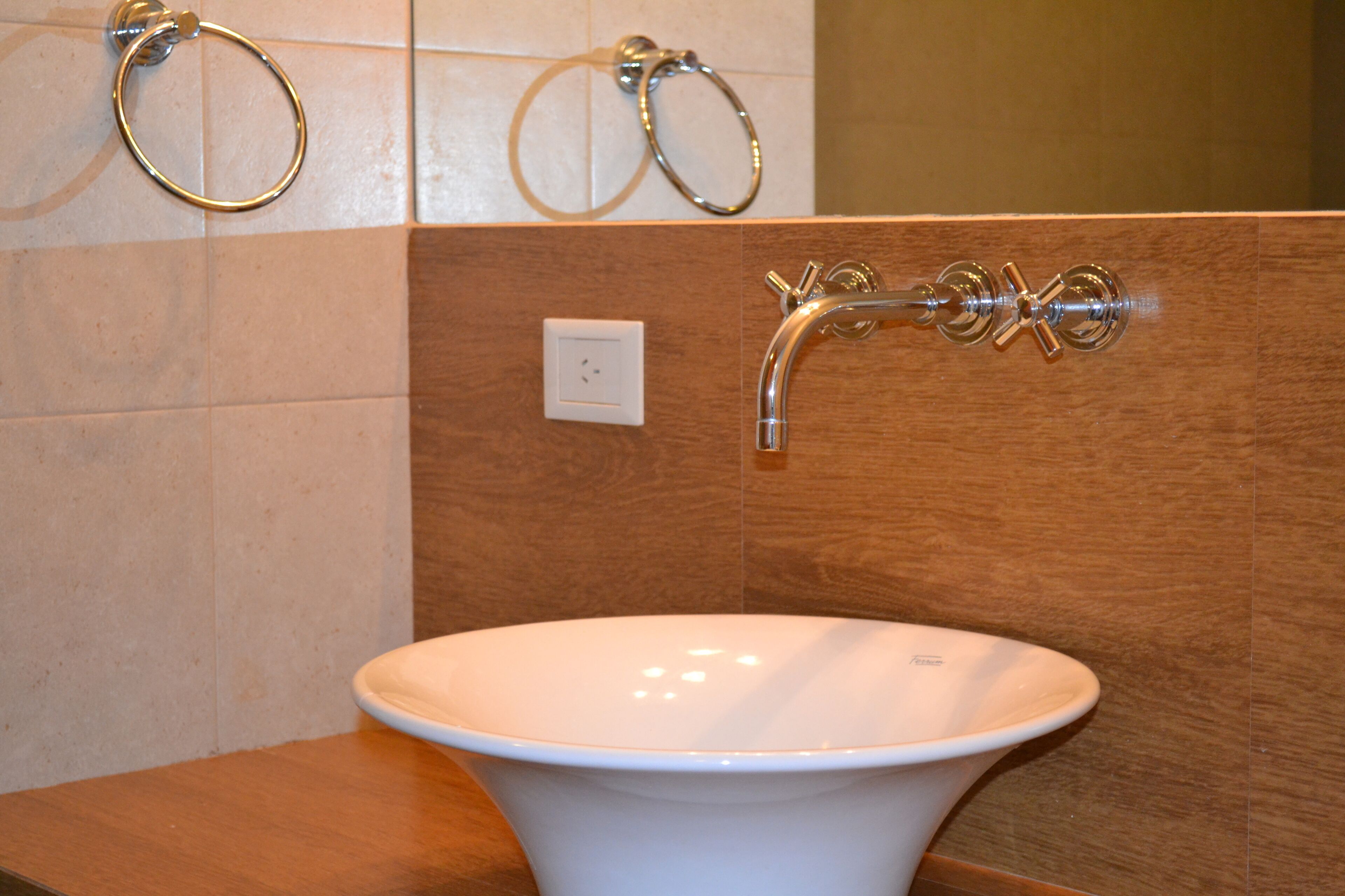 Un baño con un lavamanos blanco, un grifo cromado y dos argollas para toallas en la pared.