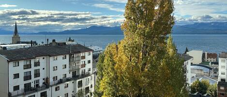 A building with multiple floors, balconies, and a view of a body of water and mountains in the background.