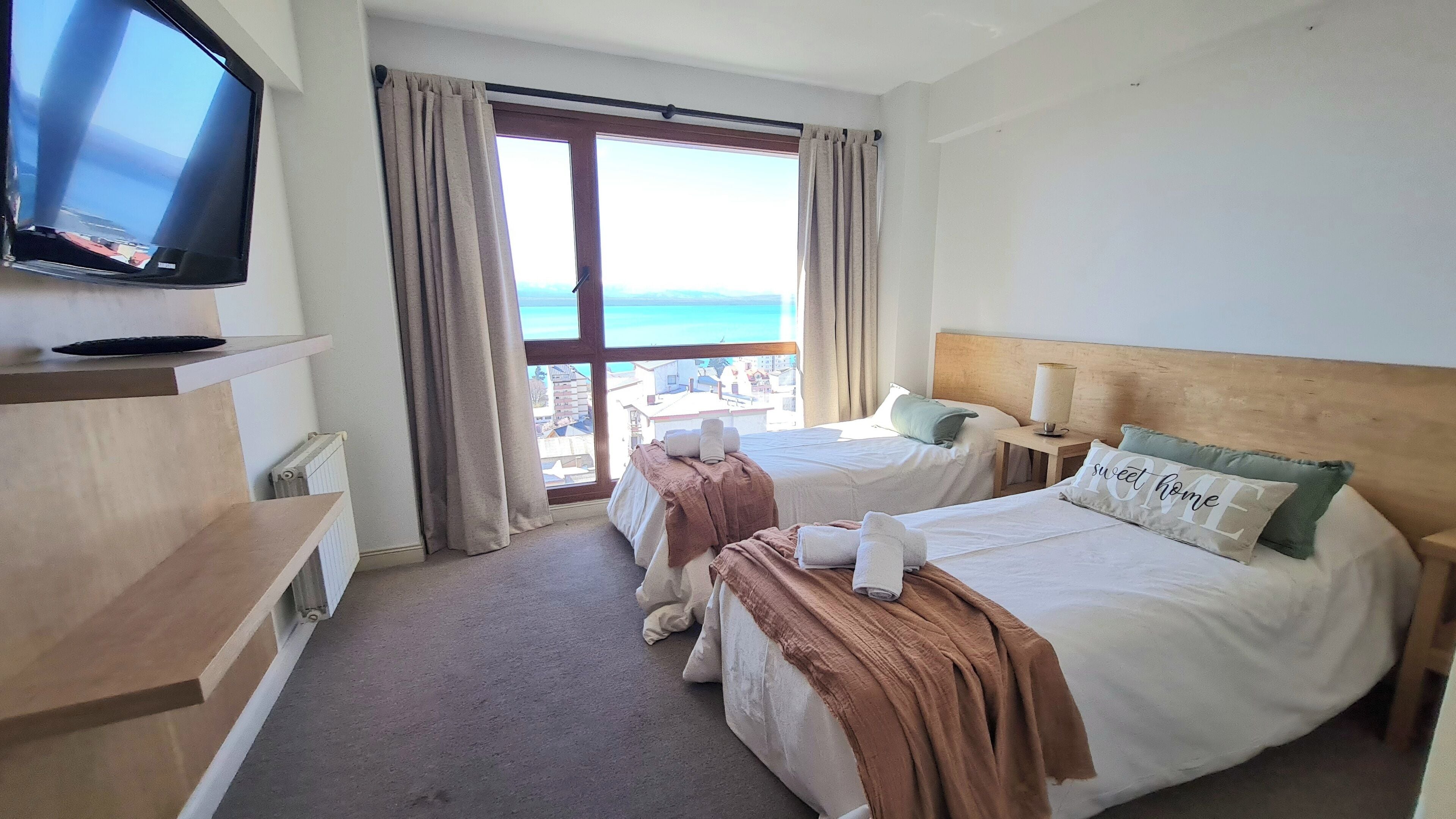 Ein Hotelzimmer mit zwei Betten, einem Fernseher an der Wand und Meerblick.