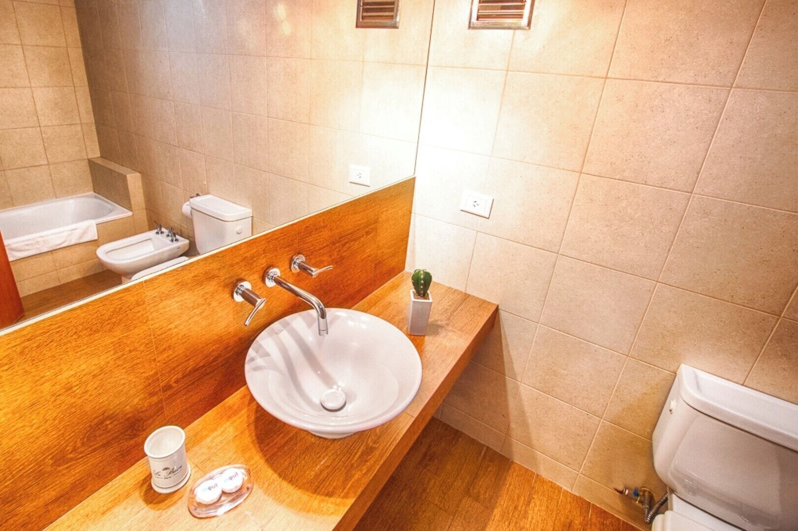 A bathroom with a wooden vanity, a white sink, a bidet, and a toilet.