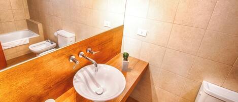 A bathroom with a wooden vanity, a white sink, a bidet, and a toilet.