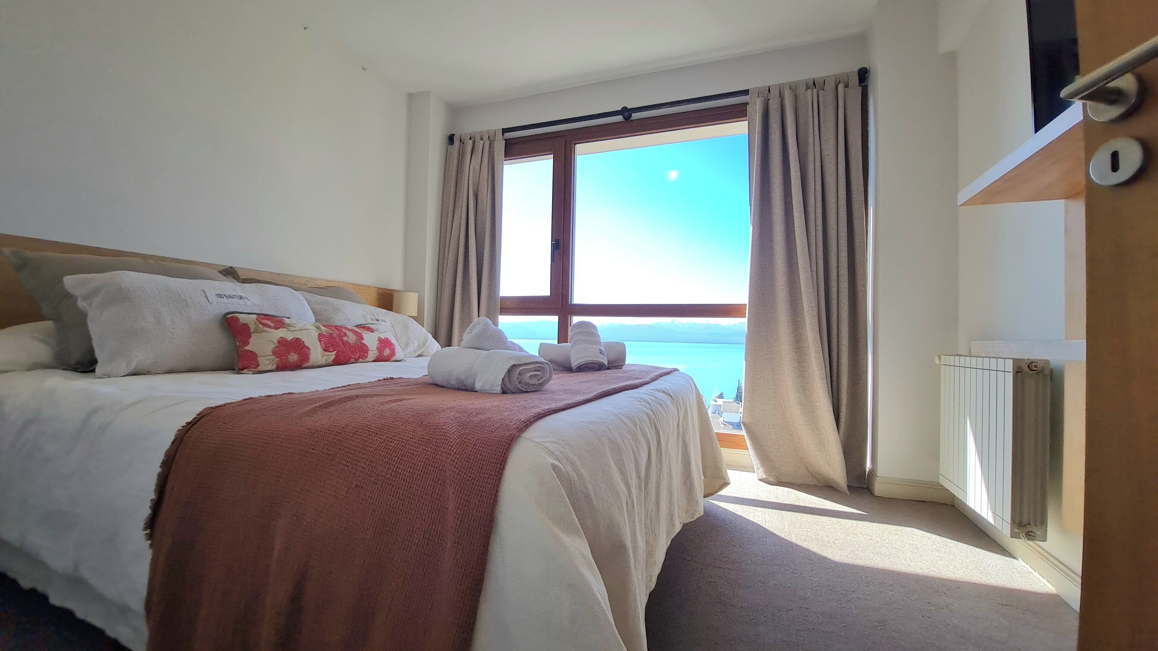Habitación de hotel con una cama, vista al mar y una ventana con cortinas.