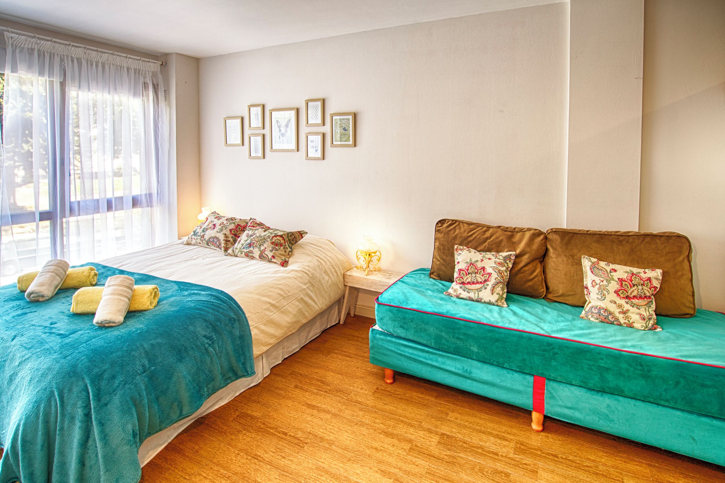 A bedroom with two beds, a window with curtains, and framed pictures on the wall.