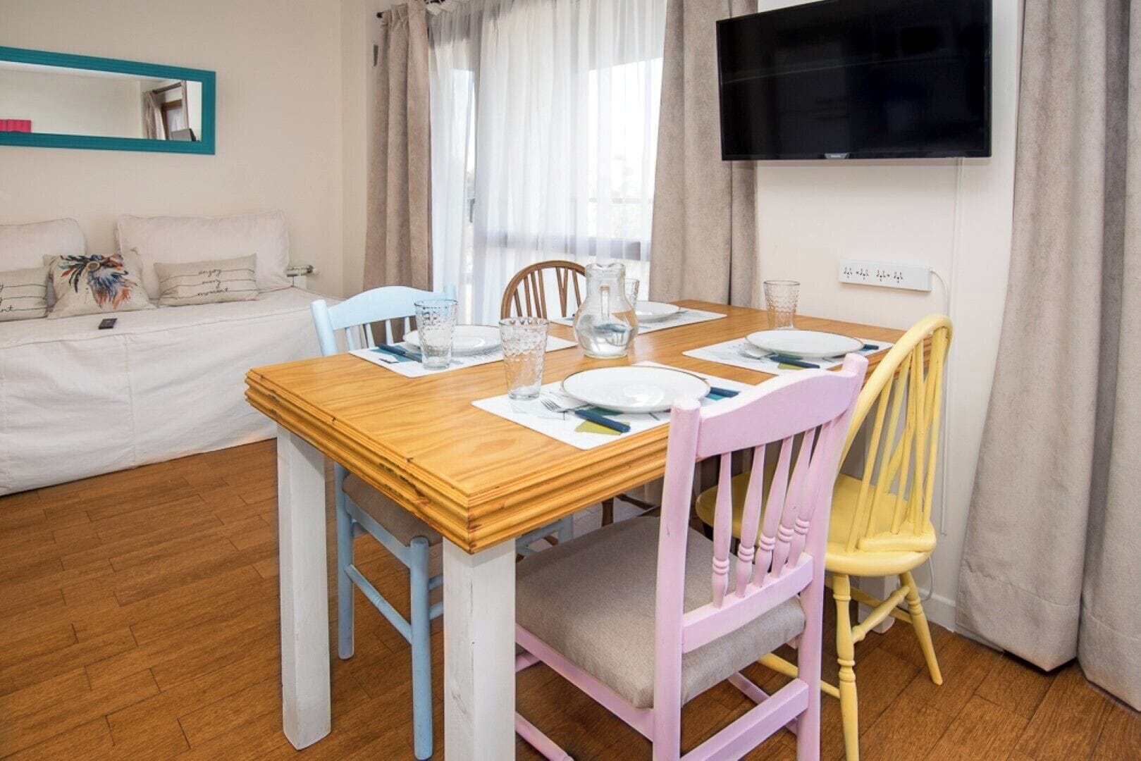 Een eetgedeelte met een houten tafel gedekt voor vier personen, omringd door pastelkleurige stoelen.