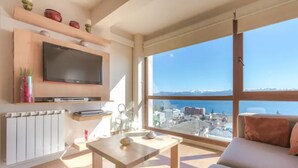 A modern living room with a large window, a flat-screen TV, and a view of a coastal city. - Terrazas I y II (San Carlos de Bariloche)