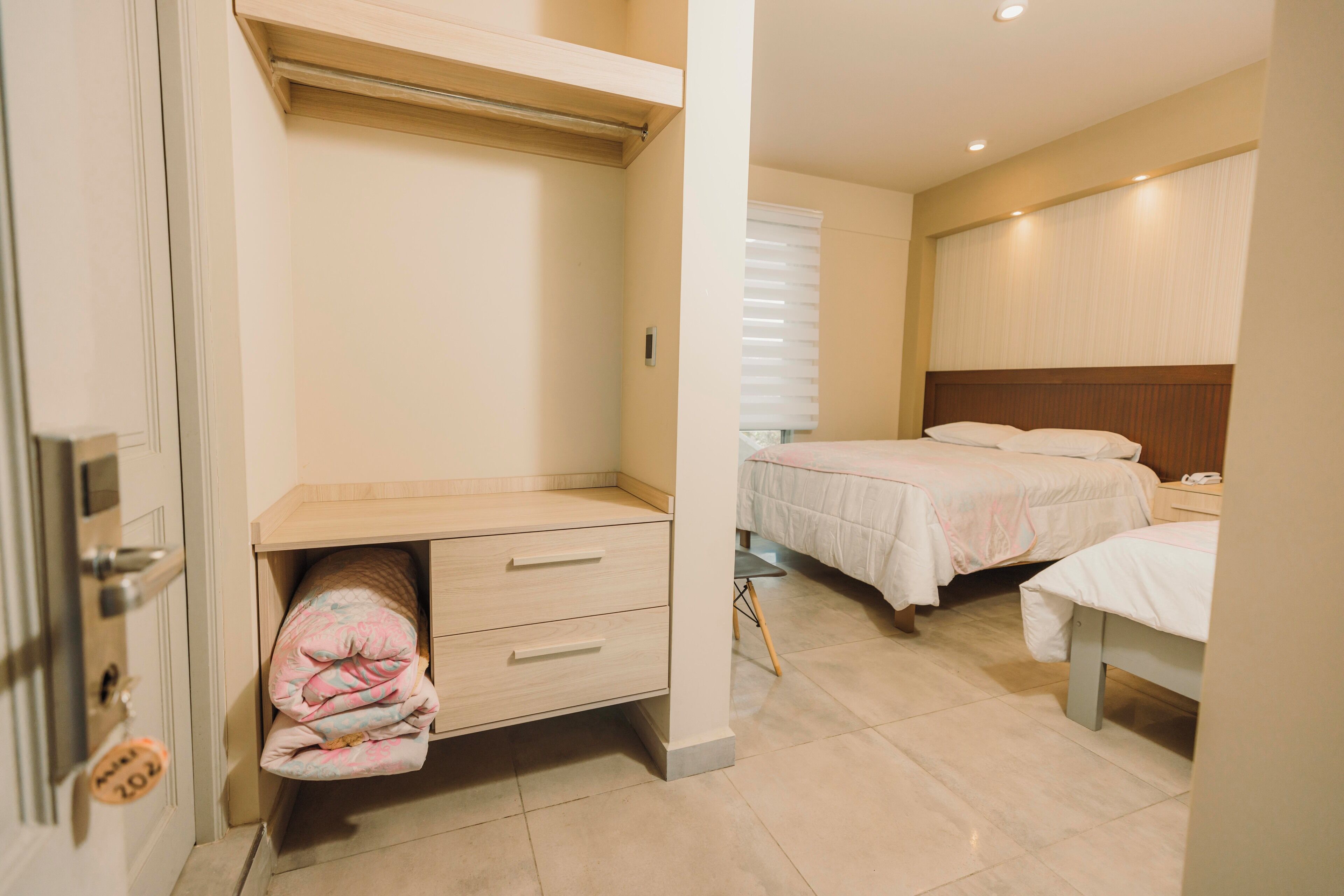Habitación de hotel con cama, mesita de noche, armario y pequeño escritorio con cajones.