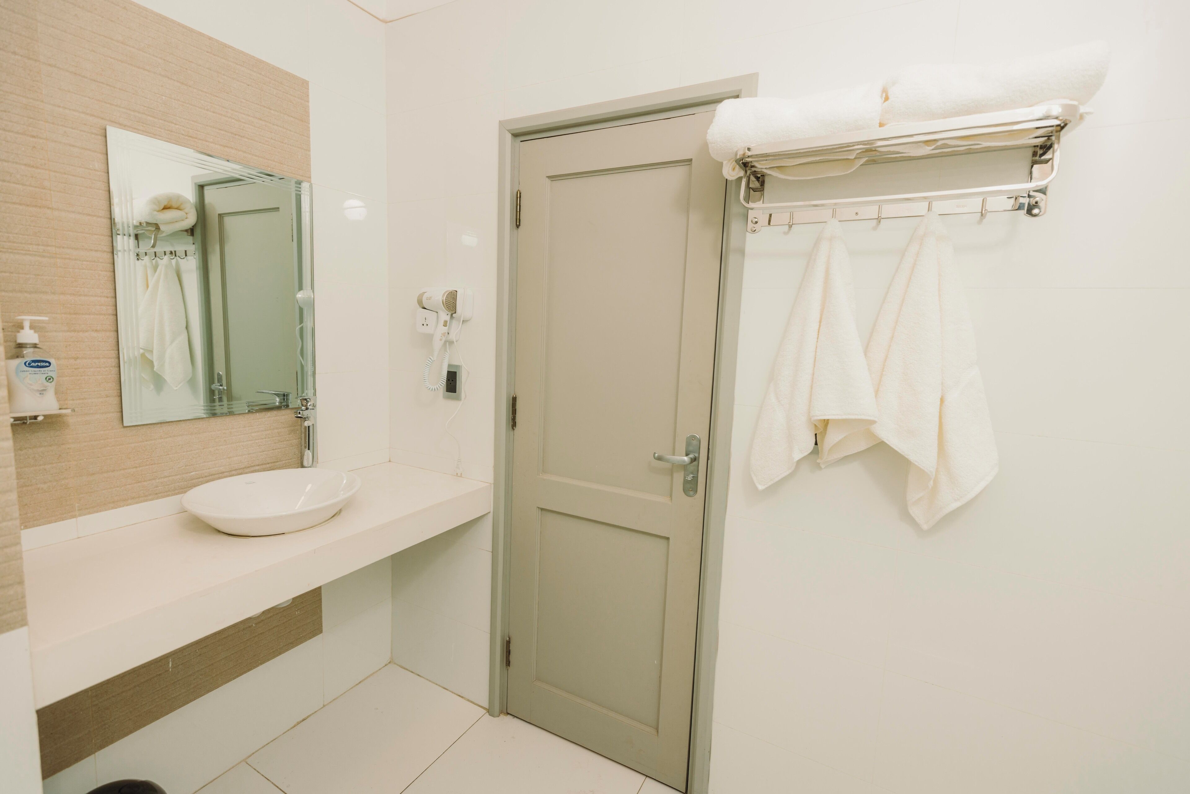 Un baño con lavamanos, espejo, toallero y una puerta.