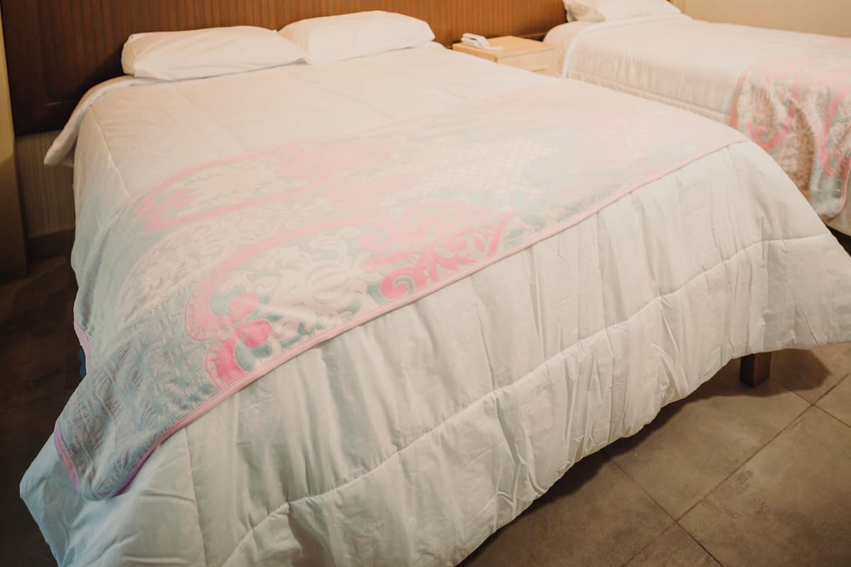 A hotel room with two beds, a wooden headboard, and a plain wall.