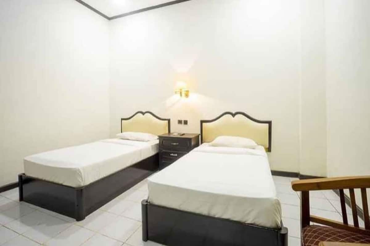 A hotel room with two single beds, a nightstand, and a wall-mounted lamp.