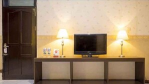 Hotellin vastaanottotila, jossa on televisiotaulussa oleva televisio, kaksi lamppua ja ovi.