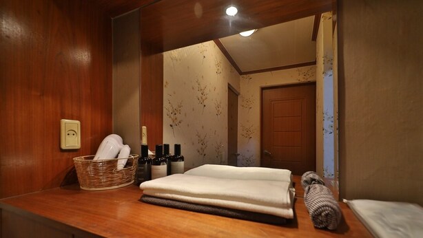 A wooden bathroom vanity with a mirror, a basket of toiletries, and neatly folded towels. - Thema Motel (Sacheon)