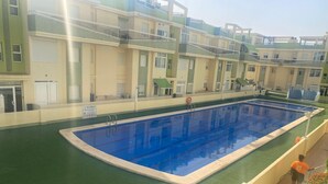 Une piscine dotée d’une plage verte, entourée d’immeubles à plusieurs étages, avec des balcons et des fenêtres.