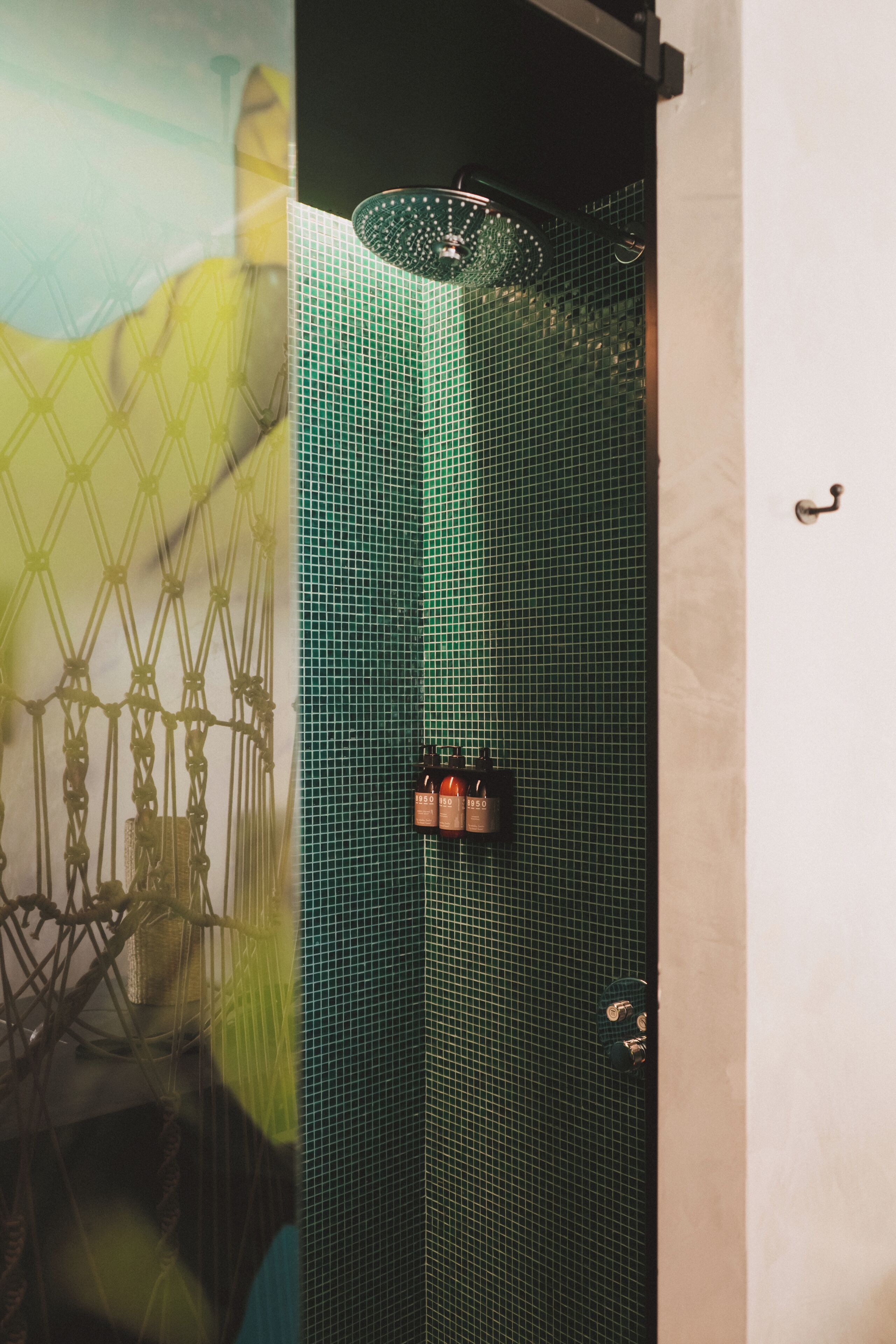 A bathroom with a green tiled shower enclosure, a towel rack, and a wall-mounted towel dispenser.