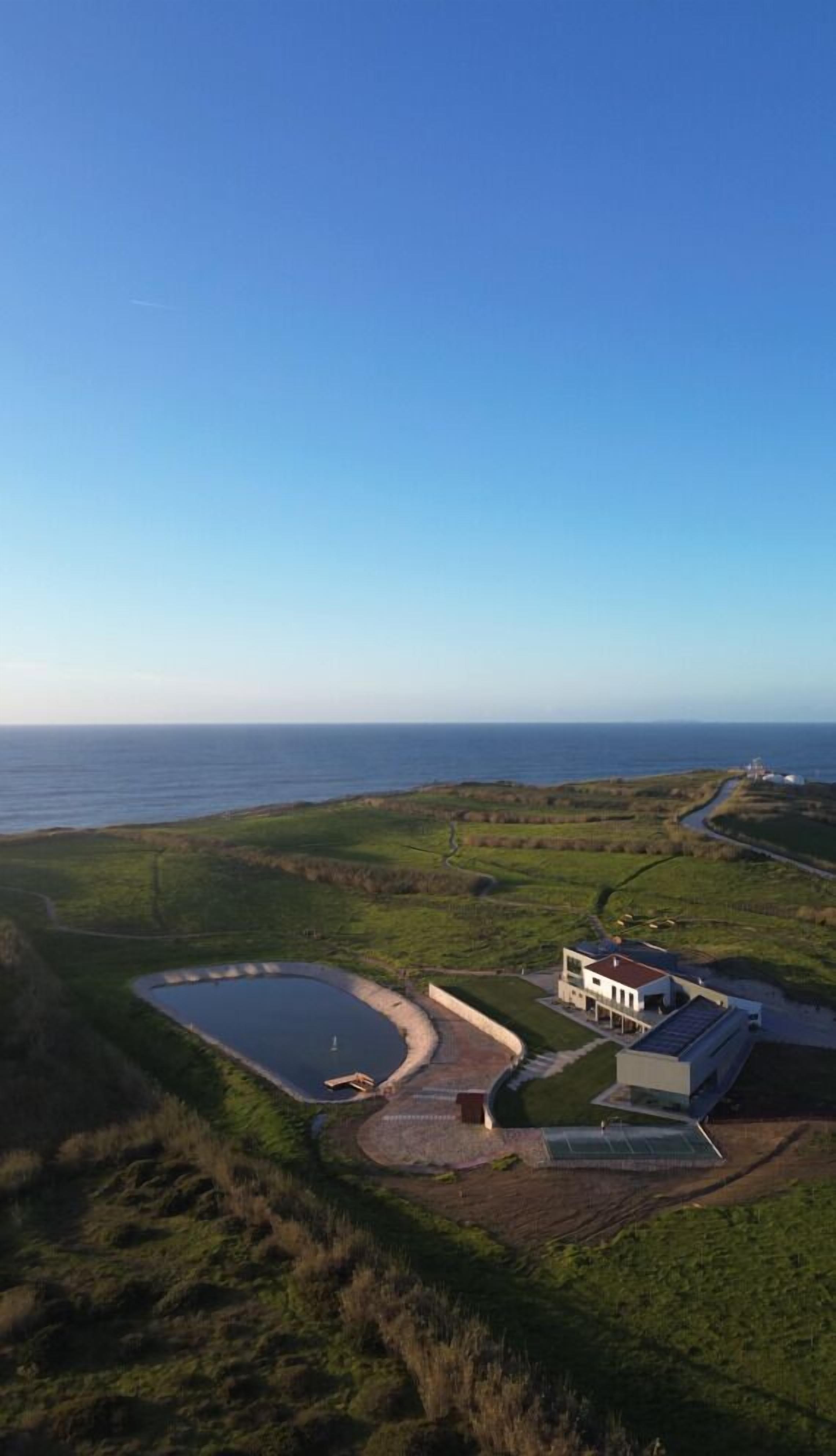 Una propiedad costera con un gran estanque, un edificio moderno y vista al mar.