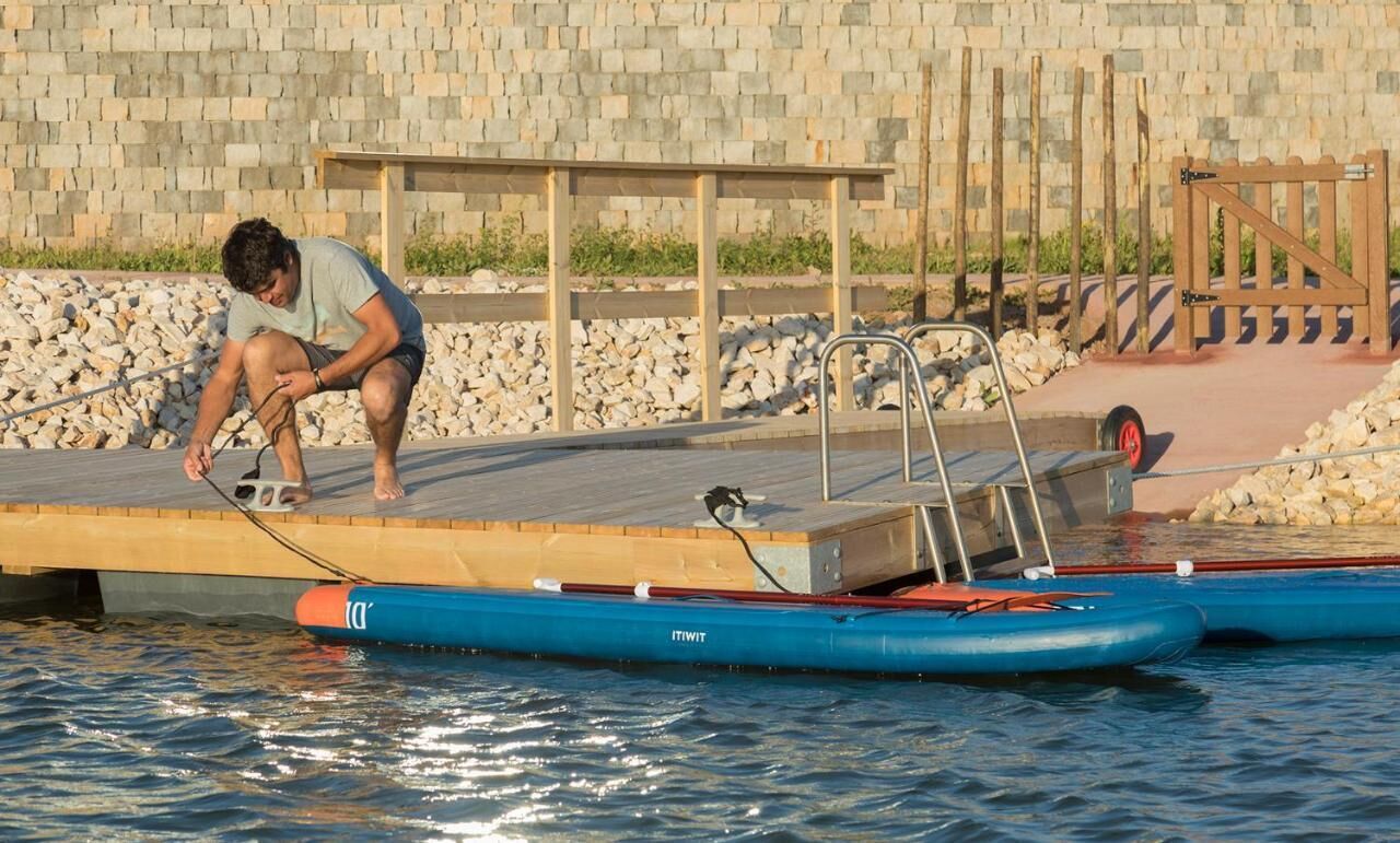 A man on a dock with a boat, a stone wall, and a wooden fence in the background.