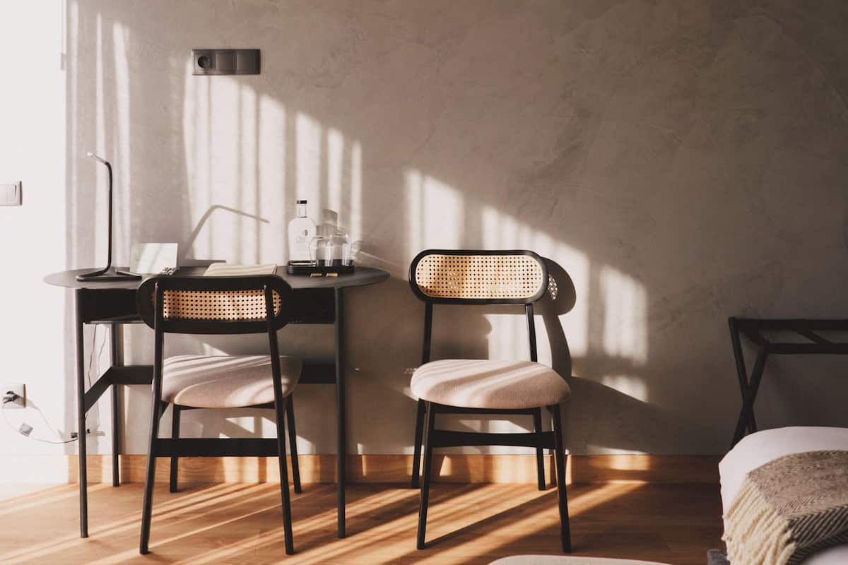 Een kamer met een houten vloer, twee stoelen, een klein tafeltje, een lamp en een bed met een deken.