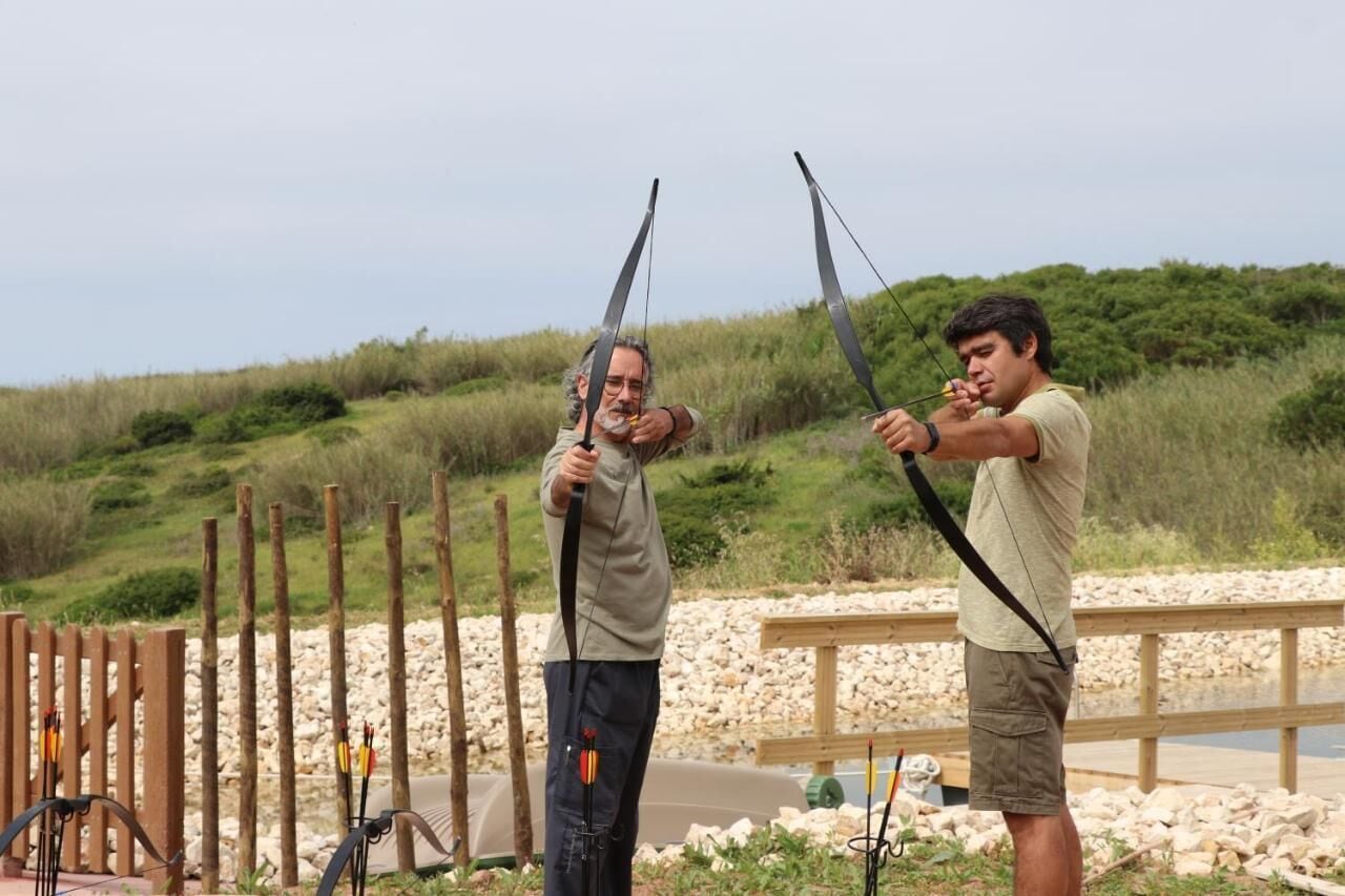 Two individuals practicing archery with bows and arrows in an outdoor setting.