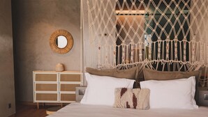 Een bed met een macramé hoofdbord, een nachtkastje, een spiegel en een dressoir.