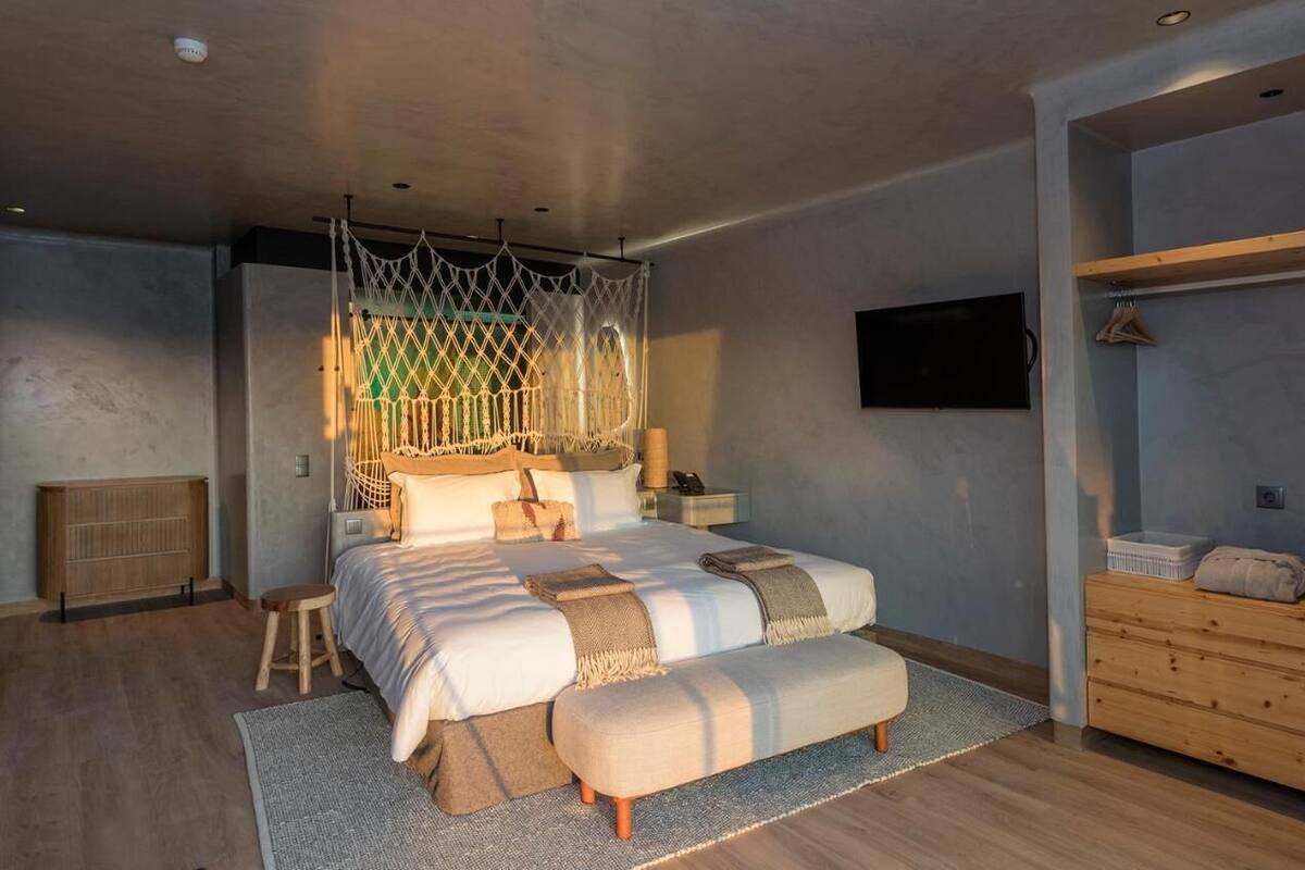 Een moderne slaapkamer met een groot bed, een houten nachtkastje, een aan de muur bevestigde televisie en een houten dressoir.